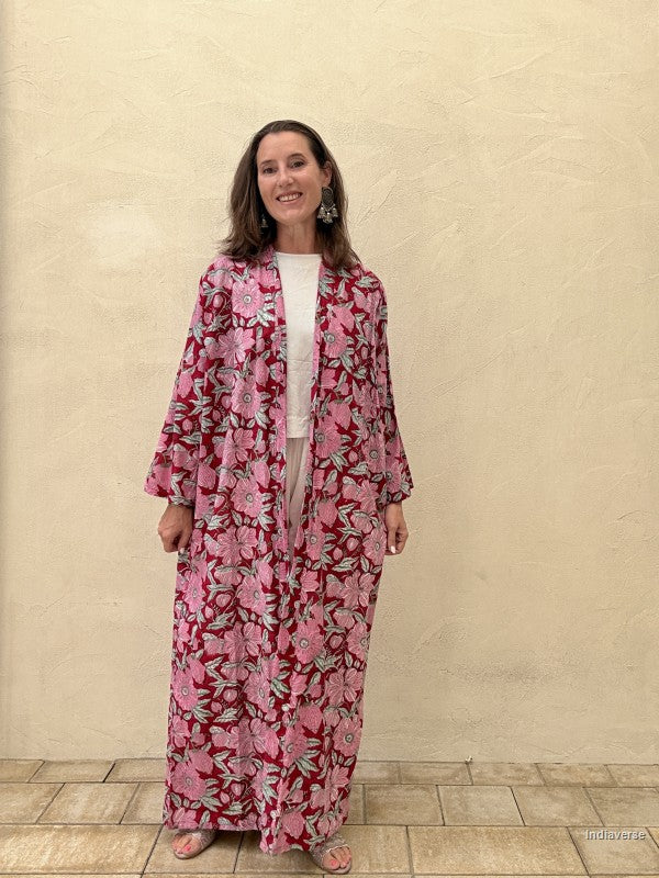 Woman wearing a pink floral kimono-style garment against a beige wall.