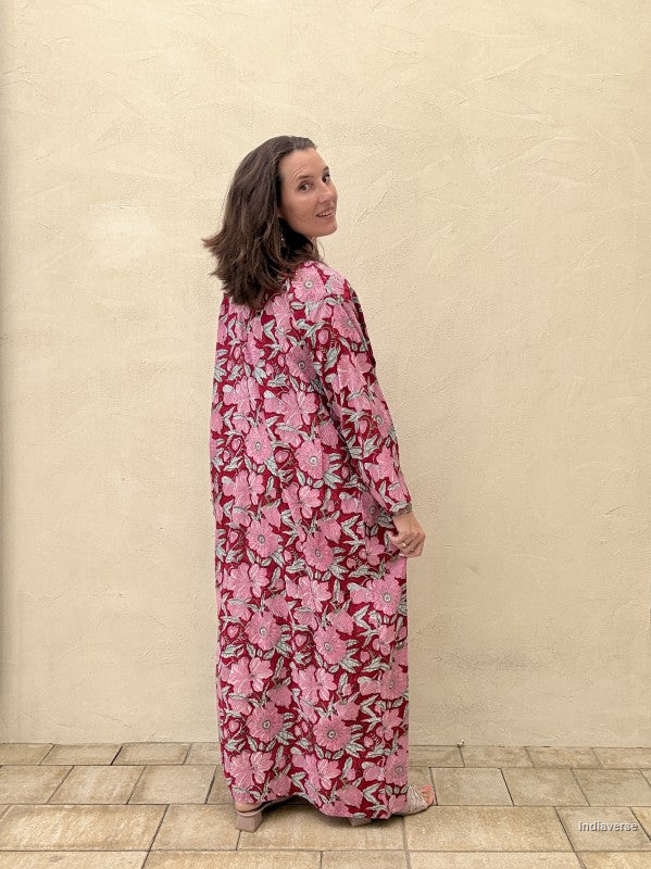 Woman wearing a pink floral dress standing against a beige wall.
