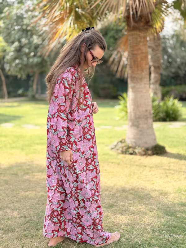 Woman in a pink floral dress standing in a garden with palm trees.
