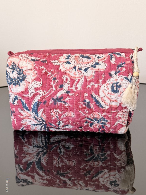 magenta colored toiletry pouch with white flowers sitting on a glass surface