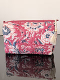 magenta colored toiletry pouch with white flowers sitting on a glass surface