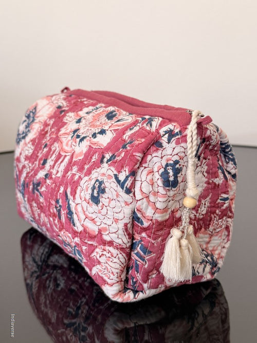 Pink floral-patterned bag with tassels on a reflective surface