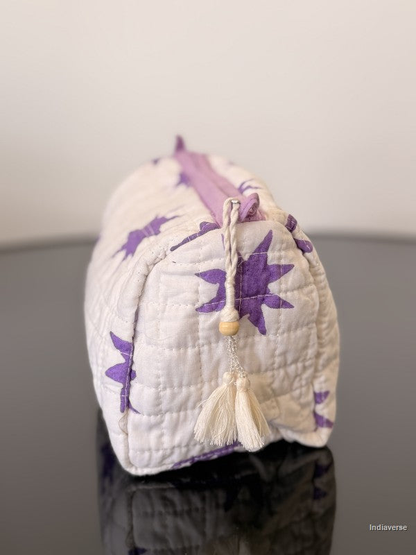 White pouch with purple floral patterns and a tassel on a reflective surface.