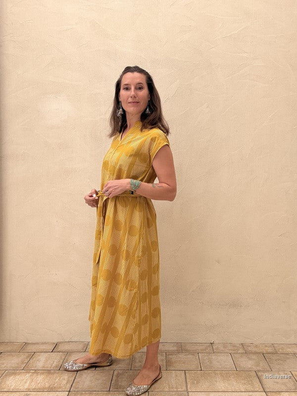 woman wearing a midi size yellow ochre dress with geometric pattern in front of a beige wall