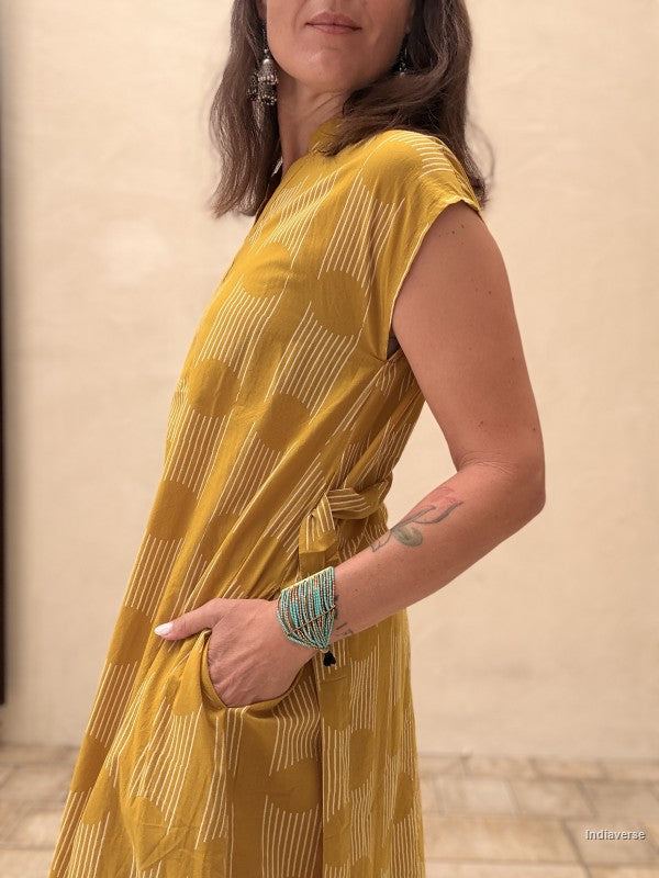 Woman wearing a yellow patterned dress against a beige wall.