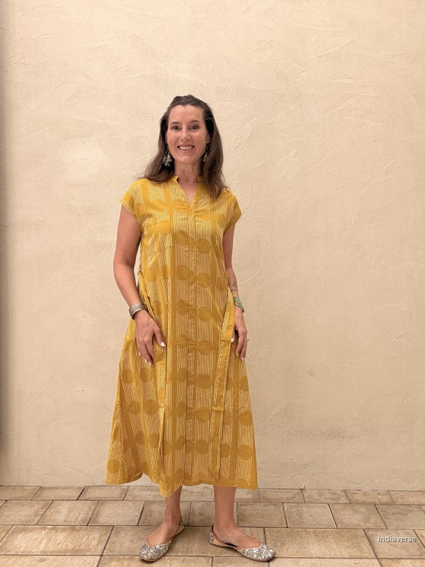 Woman wearing a yellow dress standing against a beige wall.