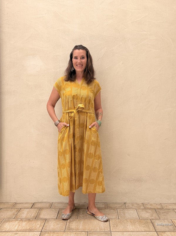 Woman wearing a yellow dress standing against a beige wall.