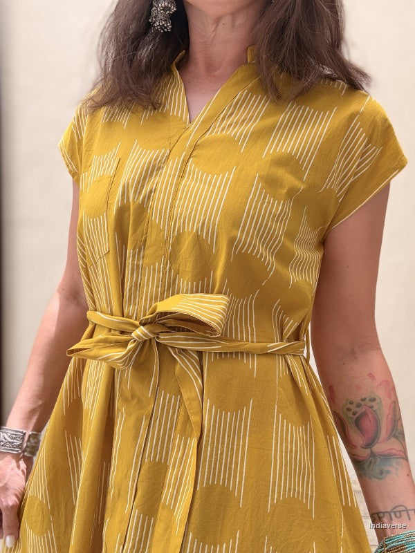 close up of the belt and midi size yellow ochre dress with geometric pattern in front of a beige wall