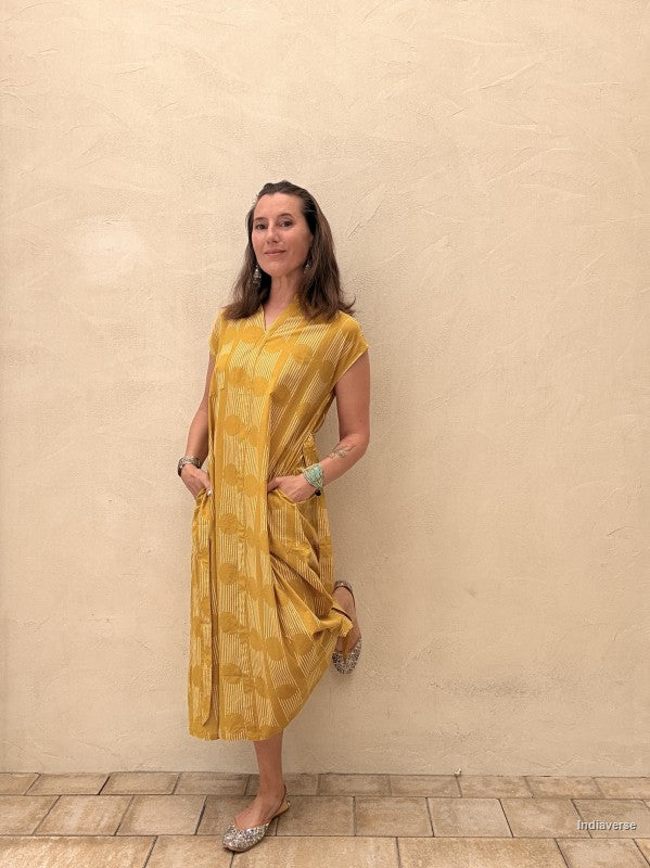 Woman wearing a yellow dress standing against a beige wall.