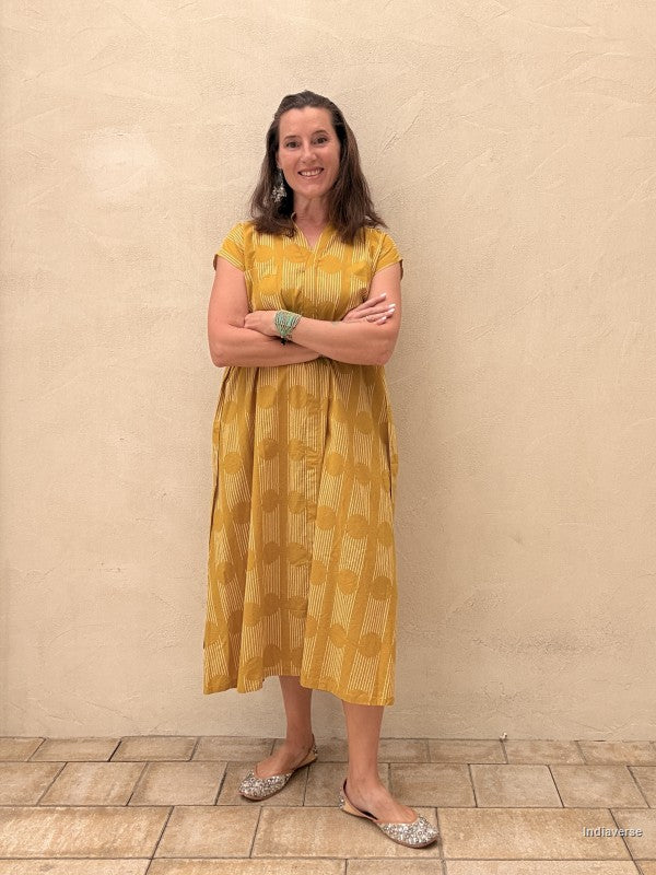 Woman wearing a yellow dress standing against a beige wall.