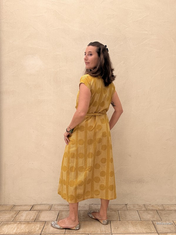 woman wearing a midi size yellow ochre dress with geometric pattern in front of a beige wall