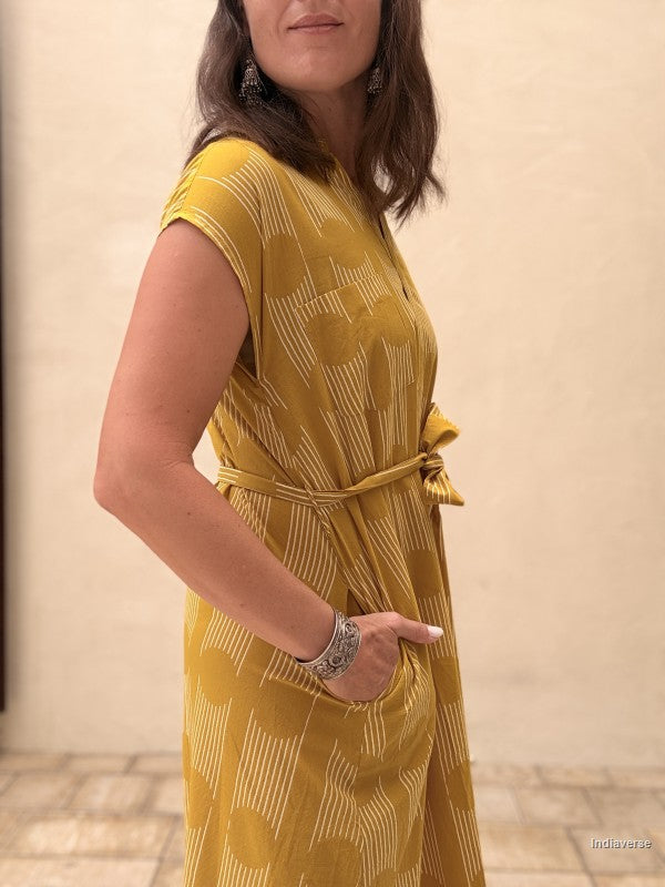 woman wearing a midi size yellow ochre dress with geometric pattern in front of a beige wall