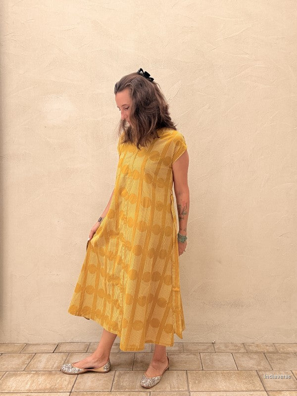 Woman wearing a yellow patterned dress against a beige wall.