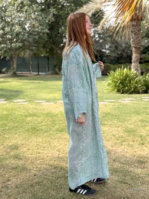 Woman wearing a long light blue dress standing on grass with trees in the background