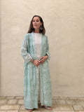Woman wearing a light green patterned dress against a beige wall.