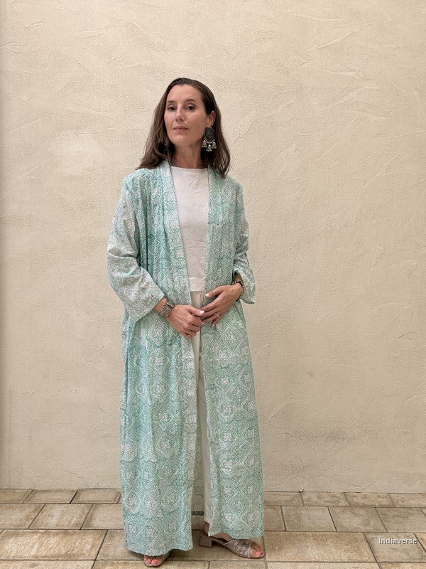 Woman wearing a light green patterned dress against a beige wall.