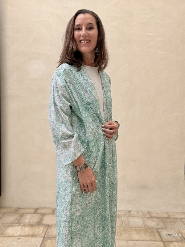 Woman wearing a light green patterned dress against a beige wall.