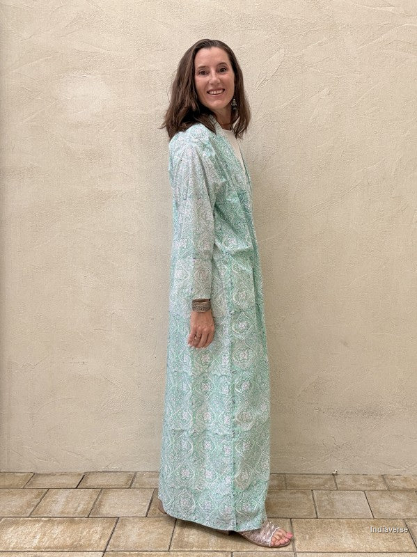 Woman wearing a light blue floral dress standing against a beige wall.