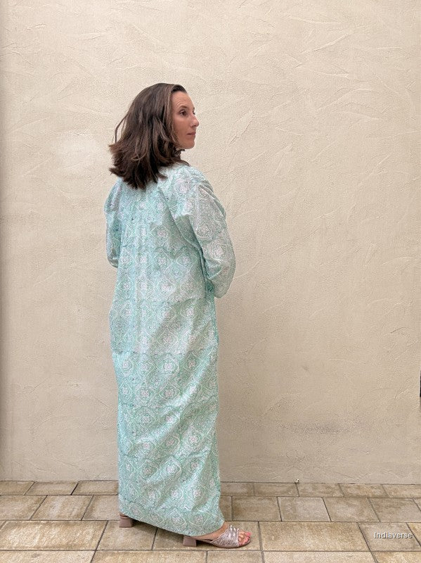 Woman wearing a light blue floral dress standing against a beige wall.