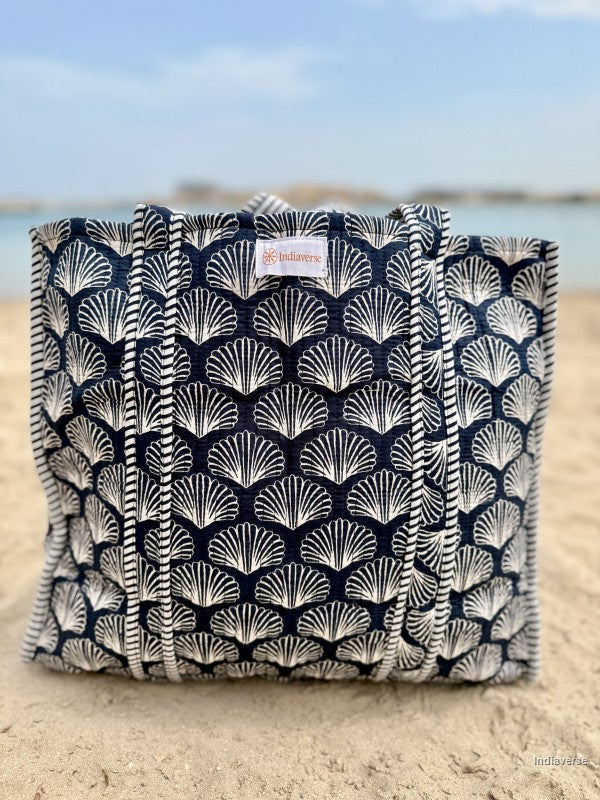 Navy blue tote bag with white shell pattern on a sandy beach