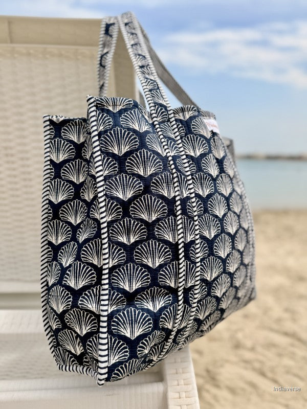 Black and white shell-patterned tote bag on a beach chair with ocean view