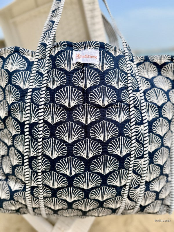Navy blue tote bag with white shell pattern on a beach setting