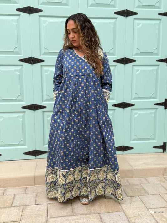 woman wearing royal blue colored festive wrap dress with silver border neckline and paisley borders at the trim and sleeves in front of a light blue door