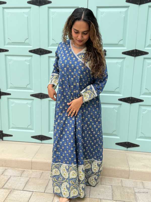 woman wearing royal blue colored festive wrap dress with silver border neckline and paisley borders at the trim and sleeves in front of a light blue door