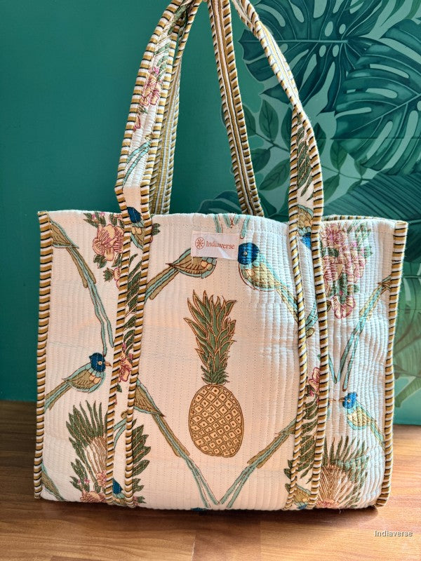 Tote bag with pineapple and bird motif standing in front of a green wall
