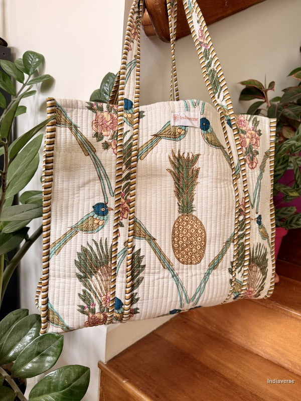 white quilted tote bag with pineapple and birds hanging from a wooden beam