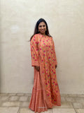 Woman wearing a peach-colored traditional outfit with floral patterns against a beige wall.