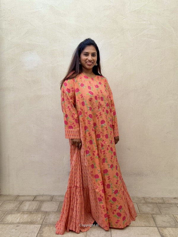 Woman wearing a floral dress standing against a plain wall.