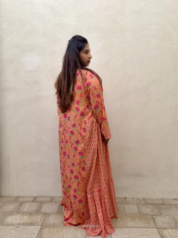 Woman wearing a long, floral-patterned dress against a plain wall.