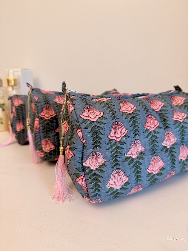 A blue fabric pouch with a pink and green floral print, featuring a pink tassel zipper pull, shown alongside two similar pouches in the background on a light beige surface | Pink Lotus
