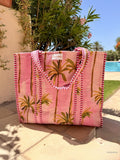 Pink tote bag with palm tree design on a patio