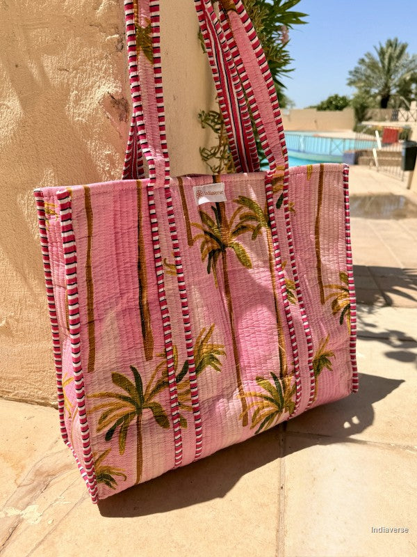 Pink tote bag with palm tree pattern on a sandy surface