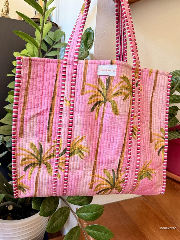 Pink tote bag with palm tree design held by a plant