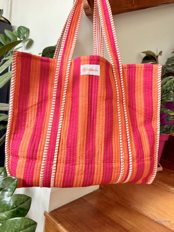 Quilted tote bag with orange and pink stripes hanging from a wooden beam