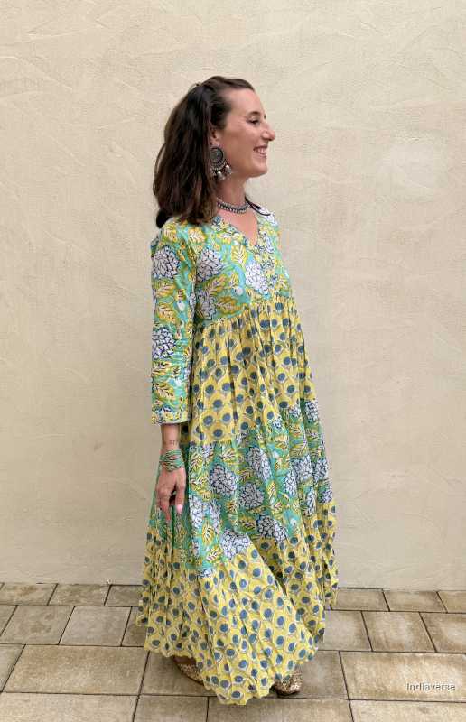 Woman wearing a long, floral dress against a beige wall.
