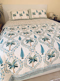 A tropical-themed quilted bedspread and matching pillow shams featuring embroidered palm trees and blue leaves on an off-white background in a well decorated bedroom.