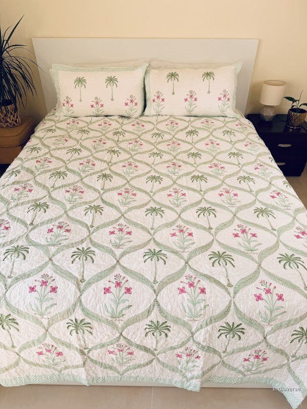 A bed dressed in a white quilted coverlet with a green trellis pattern and pink floral motifs, styled in a bedroom setting with two matching pillowcases.
