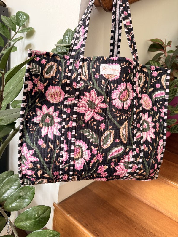 Floral patterned bag with a visible brand label on a surface with plants in the background