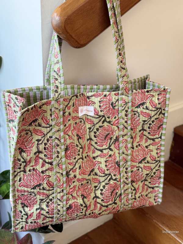 Quilted cotton tote bag in melon hue with red floral design hanging on wooden staircase railing | Spring Queen