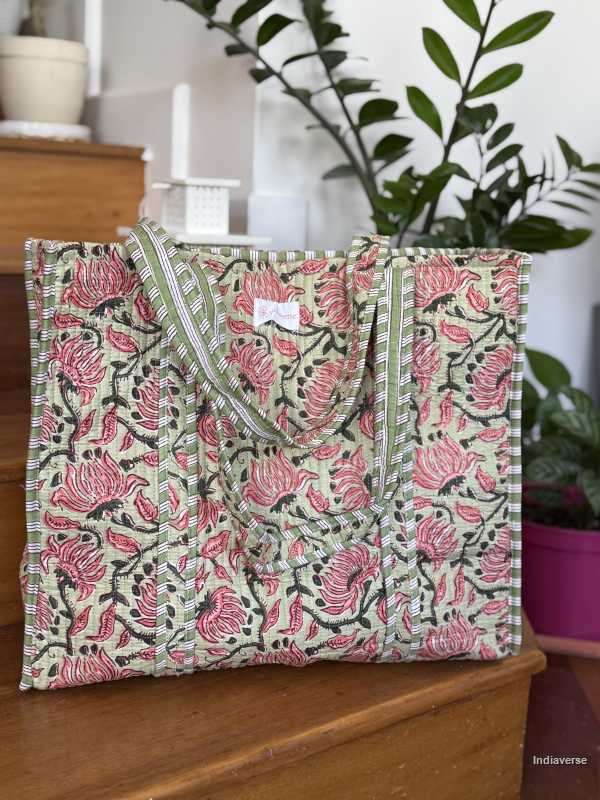 Quilted cotton tote bag in melon hue with red floral design sitting on wooden staircase with plants in background  | Spring Queen