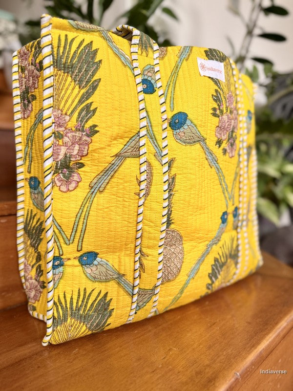 Yellow embroidered clutch bag with floral and bird patterns on a wooden surface.
