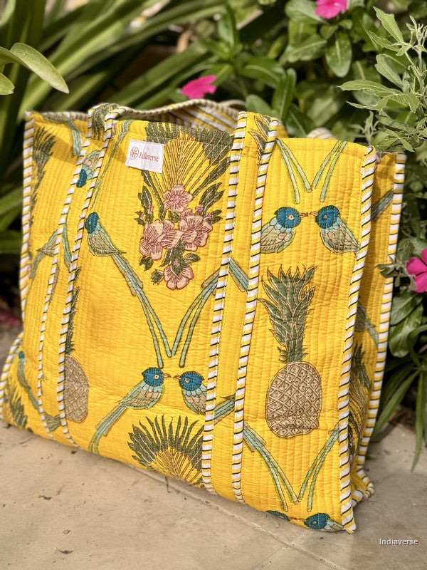 Yellow embroidered fabric bag with floral and bird patterns on a green leafy background