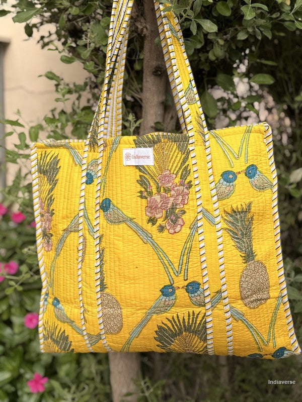 Yellow embroidered bag with floral and bird patterns held by a person outdoors.