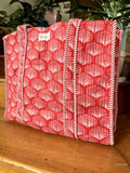Red and white sea shell bag on a wooden surface with plants in the background