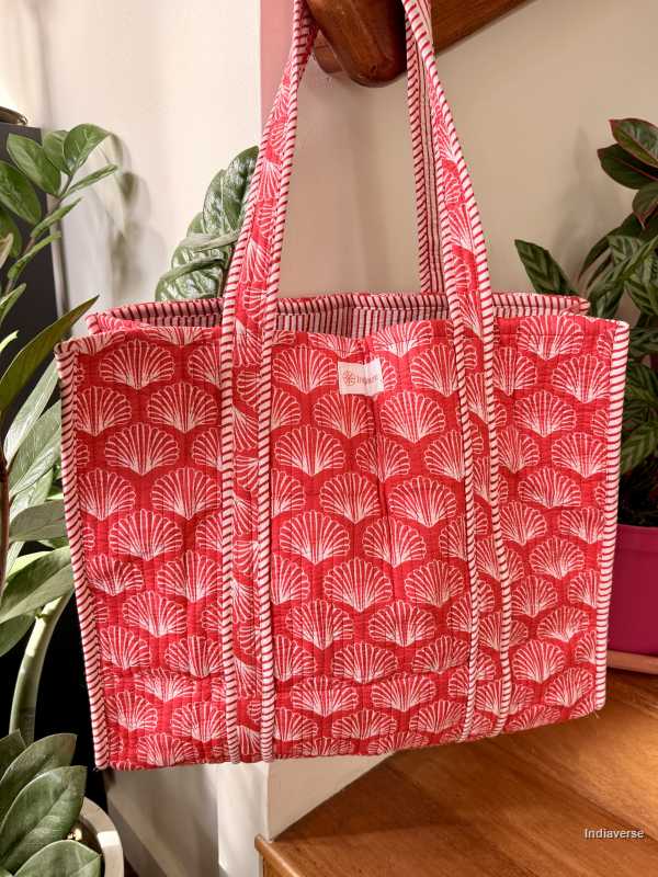 Red and white patterned tote bag hanging on a wooden surface with plants in the background