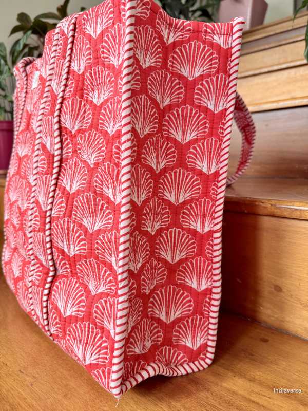 Red cotton tote bag with white shell pattern on a wooden surface